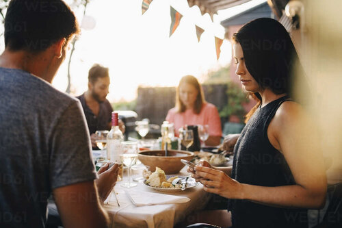 woman-using-smart-phone-while-sitting-with-friends-at-dining-table-in-dinner-party-MASF12664.jpg